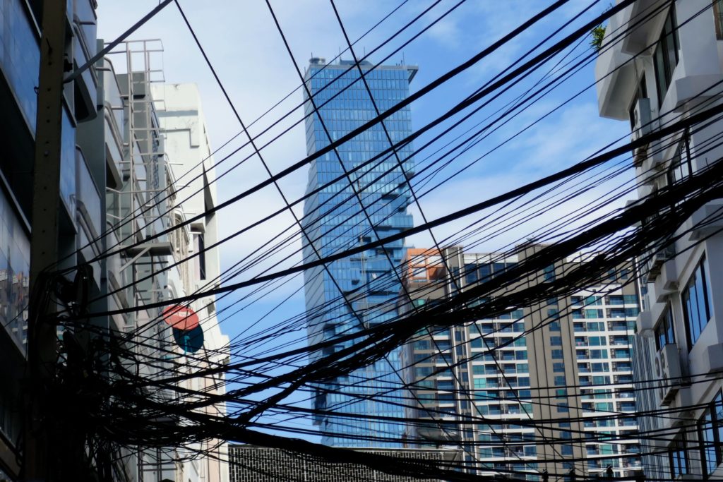 MahanaKhon Tower in Bangkok, eingerahmt von anderen Häusern, versteckt hinter Kabelgewirr.