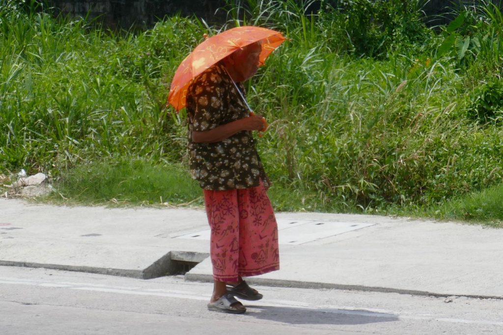 Menschen in Ranong. Alte Frau mit Schirm in der Mittagshitze.