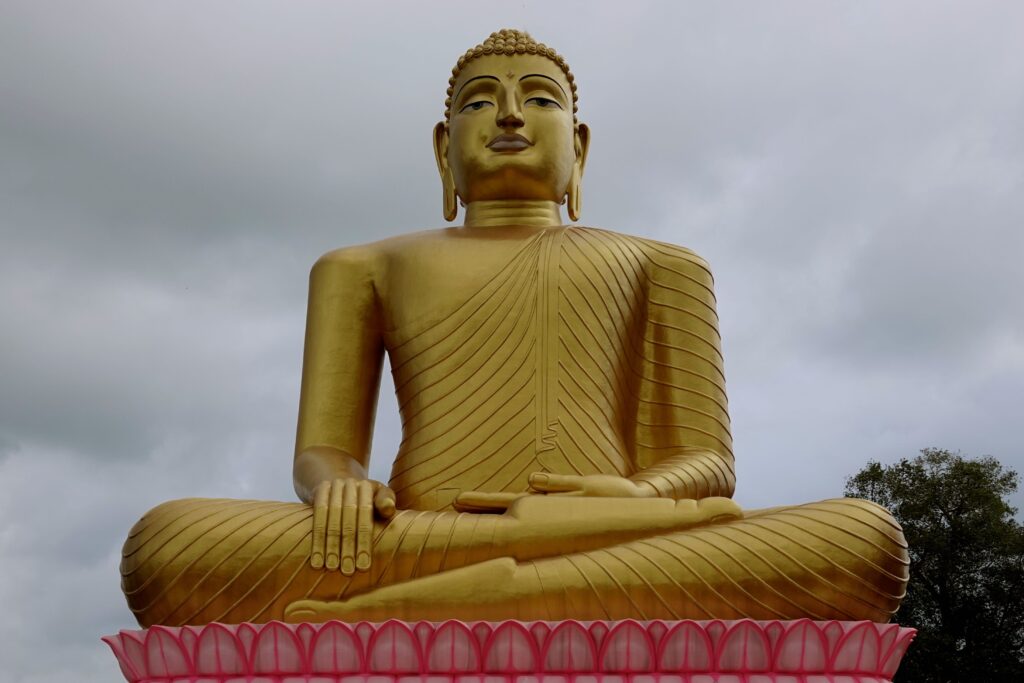 Große goldene Buddha-Statue auf rosafarbenem Lotussockel im Sri Vijayarama Vihara nahe Beruwala, Sri Lanka, vor bewölktem Himmel