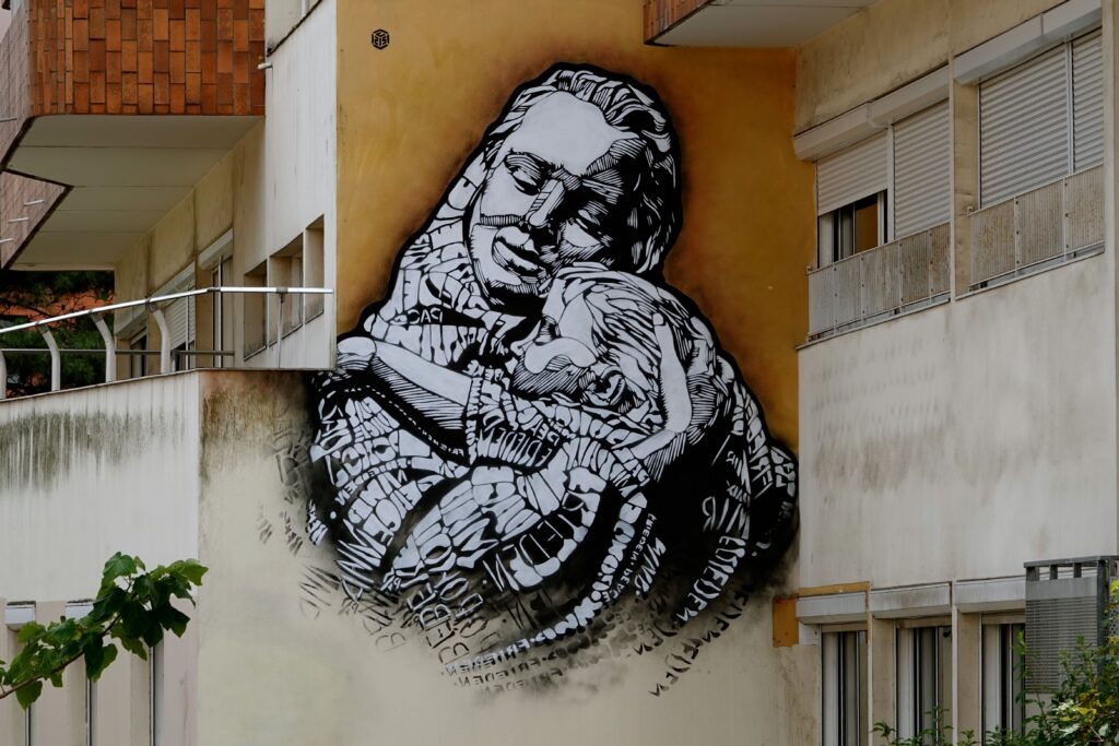 Schwarz-weißes Wandbild von C215 mit Mutter und Kind, deren Kleidung aus dem Wort "Frieden" in verschiedenen Sprachen besteht, Paris 13