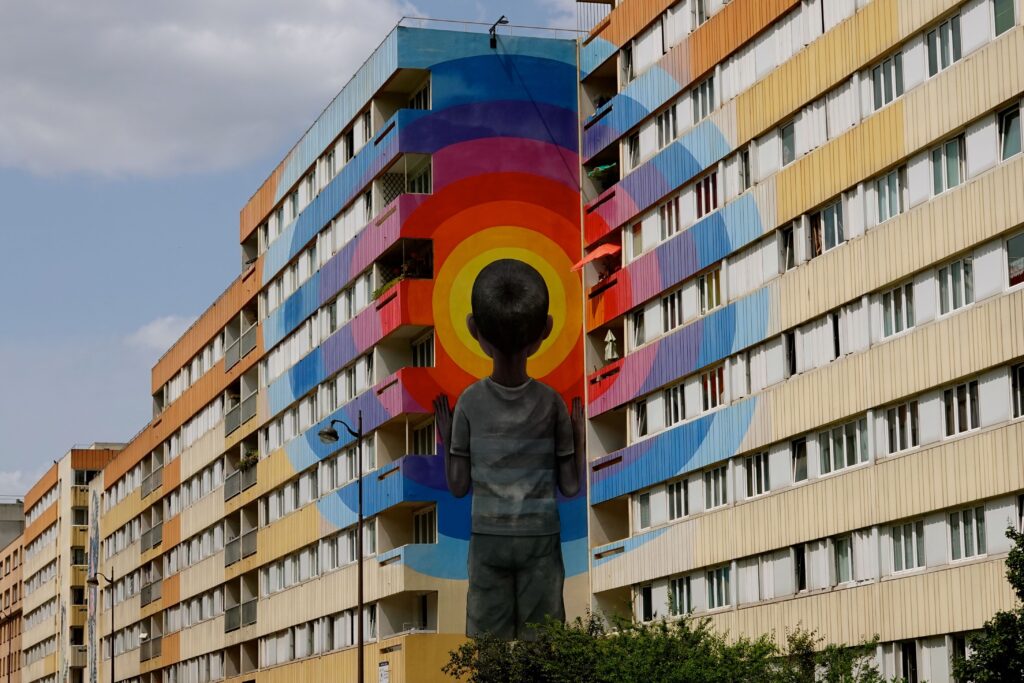 Wandgemälde von Seth (Julien Malland) mit einem Kind vor regenbogenfarbenen Gebäuden im 13. Arrondissement Paris