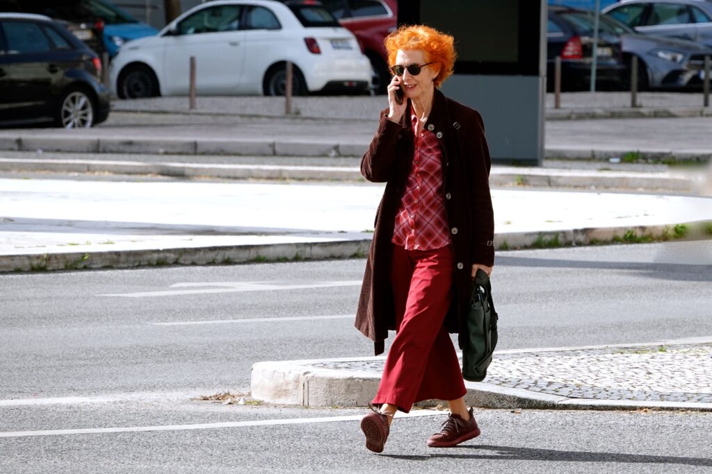 Frau mit orangefarbenen Haaren telefoniert beim Überqueren einer Straße in Alvalade, Lissabon