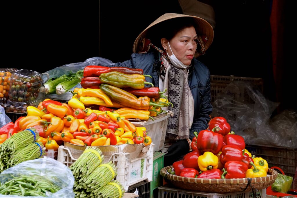 Vietnamesische Gemüsehändlerin mit bunten Paprika und Gemüse auf dem Đà Lạt Markt